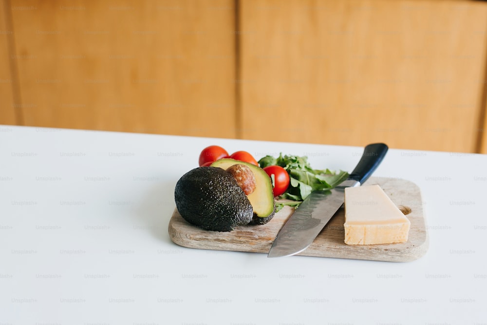 Avocado, cherry tomatoes, arugula, parmesan and knife on wooden cutting board in white modern kitchen. Process of making home avocado toast. Healthy eating and Home cooking concept