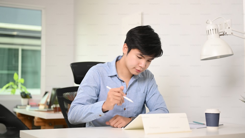 Young businessman sitting in comfortable workplace and working with digital tablet.