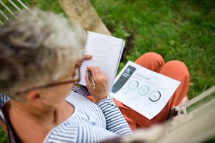 Top view of active senior woman working outdoors in garden, green home office concept.