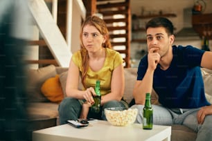 Giovane coppia che si sente preoccupata per la loro squadra sportiva preferita mentre guarda una partita in TV a casa.