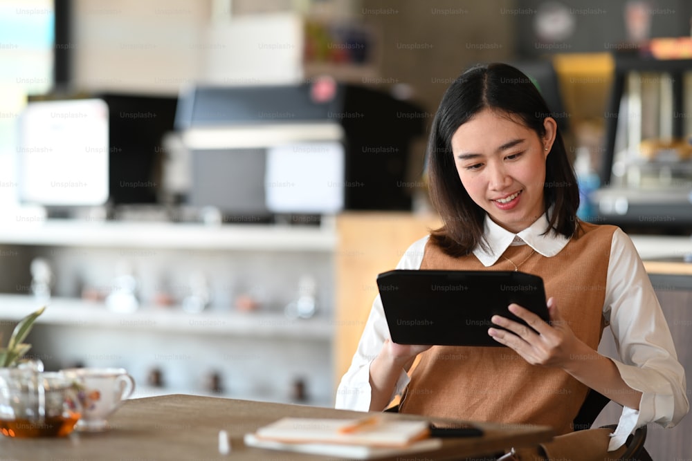 デジタルタブレットを使用し、コーヒーショップに座っている幸せな若い女性。