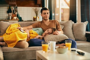 Young couple relaxing in the living room. Smiling man is watching TV while woman is sleeping n the sofa.
