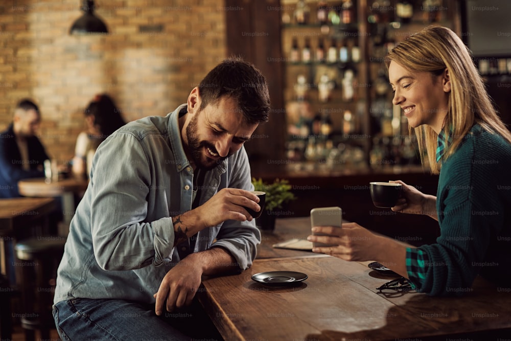 Happy couple reading something funny on smart phone while drinking coffee in a cafe.