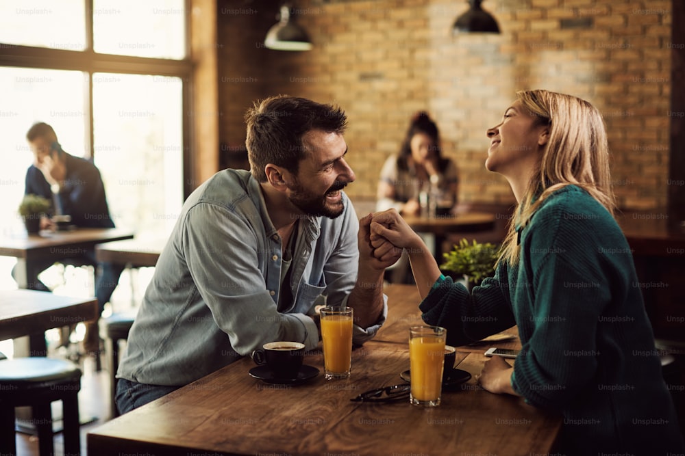 Hombre feliz coqueteando con su novia mientras la toma de la mano y habla en un café.