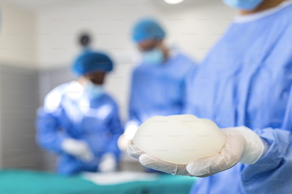Médecin tenant un implant en silicone médical. Surgent tient l’implant en silicone et l’installe dans le gros plan du buste de la femme. Concept d’entreprise d’augmentation mammaire d’intervention chirurgicale