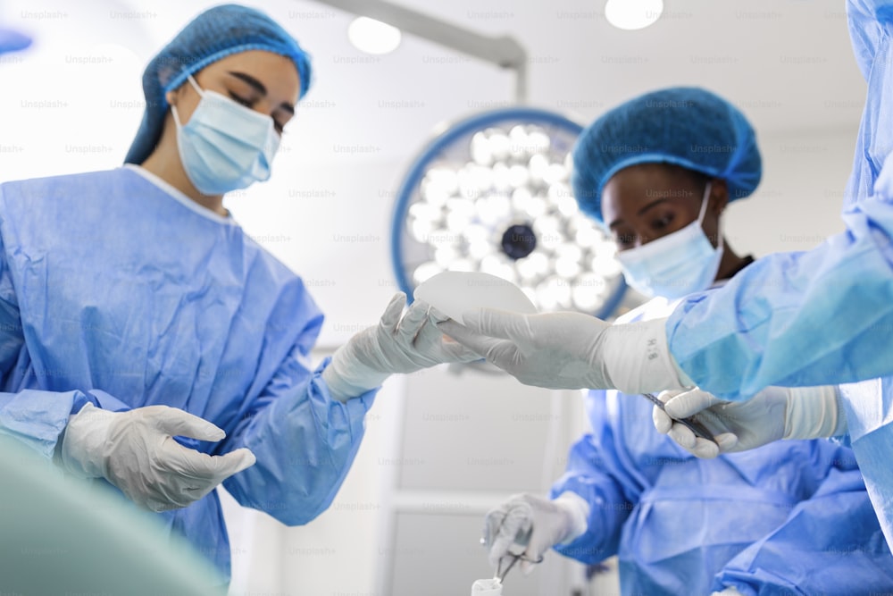 Cirurgião e seu assistente realizando cirurgia plástica em centro cirúrgico hospitalar. Cirurgião de máscara durante a procadure. Aumento de mama, alargamento, realce