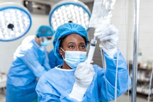 Femme afro-américaine Médecin dans la salle d’opération mettant des médicaments à travers une intraveineuse - concepts chirurgicaux