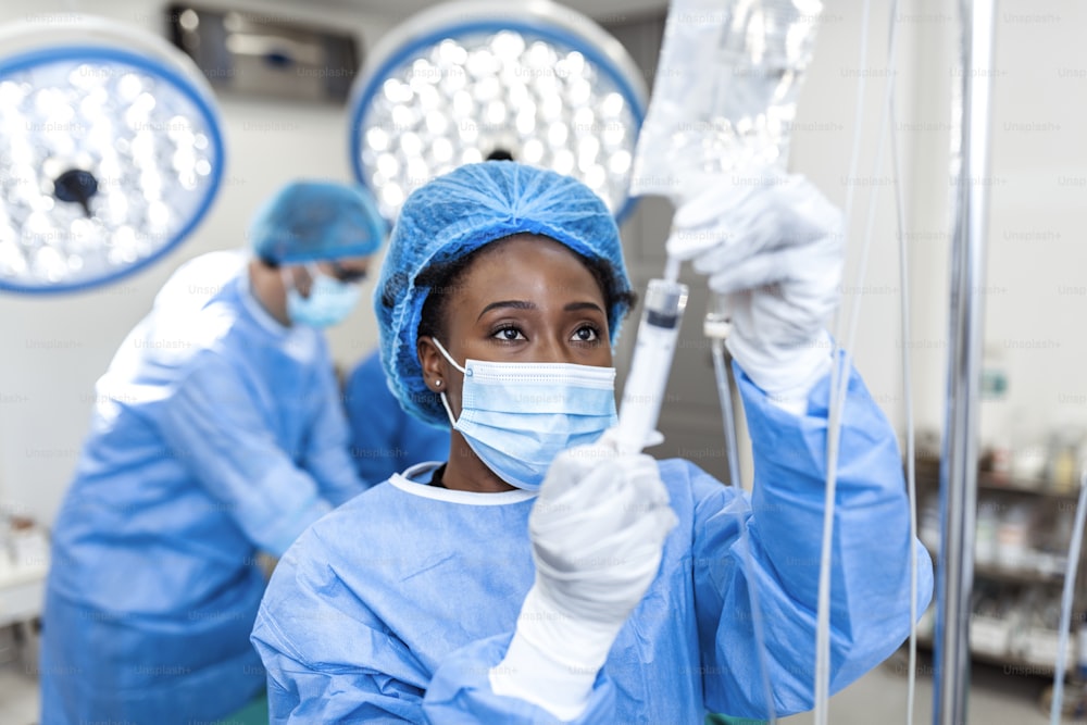 Doctora afroamericana en el quirófano que somete medicamentos a una vía intravenosa - conceptos de cirugía