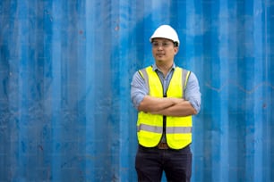 Retrato do homem de engenharia vestindo traje de segurança uniforme e capacete em recipientes industriais.
