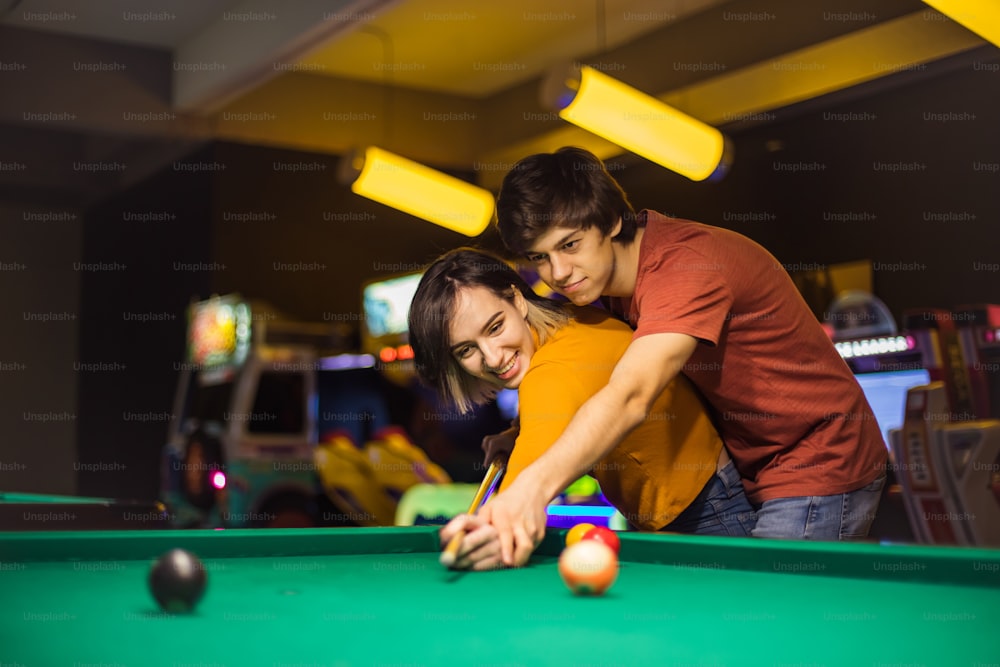 Young couple spending time in billiard room. Boyfriend teaching his girlfriend to playing billiard. Focus is on couple.