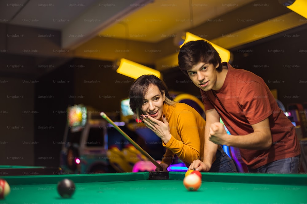 Young couple spending time in billiard room. He is her support.