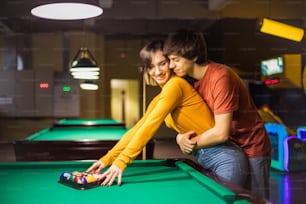 Couple in the billiard room. Couple in playroom. Man hugging his girlfriend.