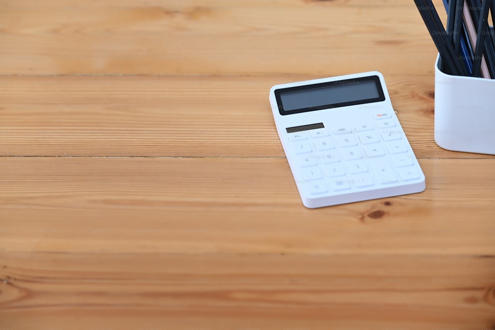 Calculator and pencils holder on wooden table at accountant workplace. Copy space