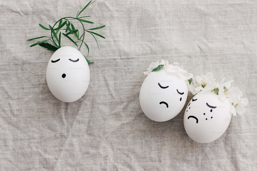 Easter concept. Natural eggs with sad crying and calm faces in cute floral wreaths on linen fabric, top view. Eco friendly zero waste holiday. Christ is risen conceptual