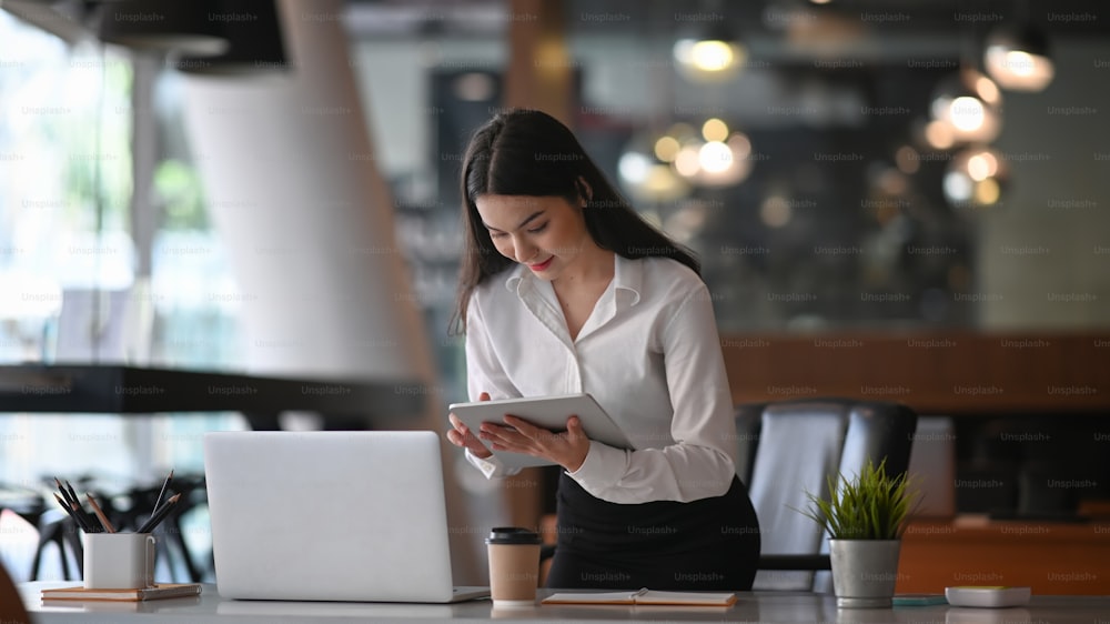 Vielbeschäftigte Geschäftsfrau, die mit einem Laptop arbeitet und Informationen auf einem digitalen Tablet sucht.