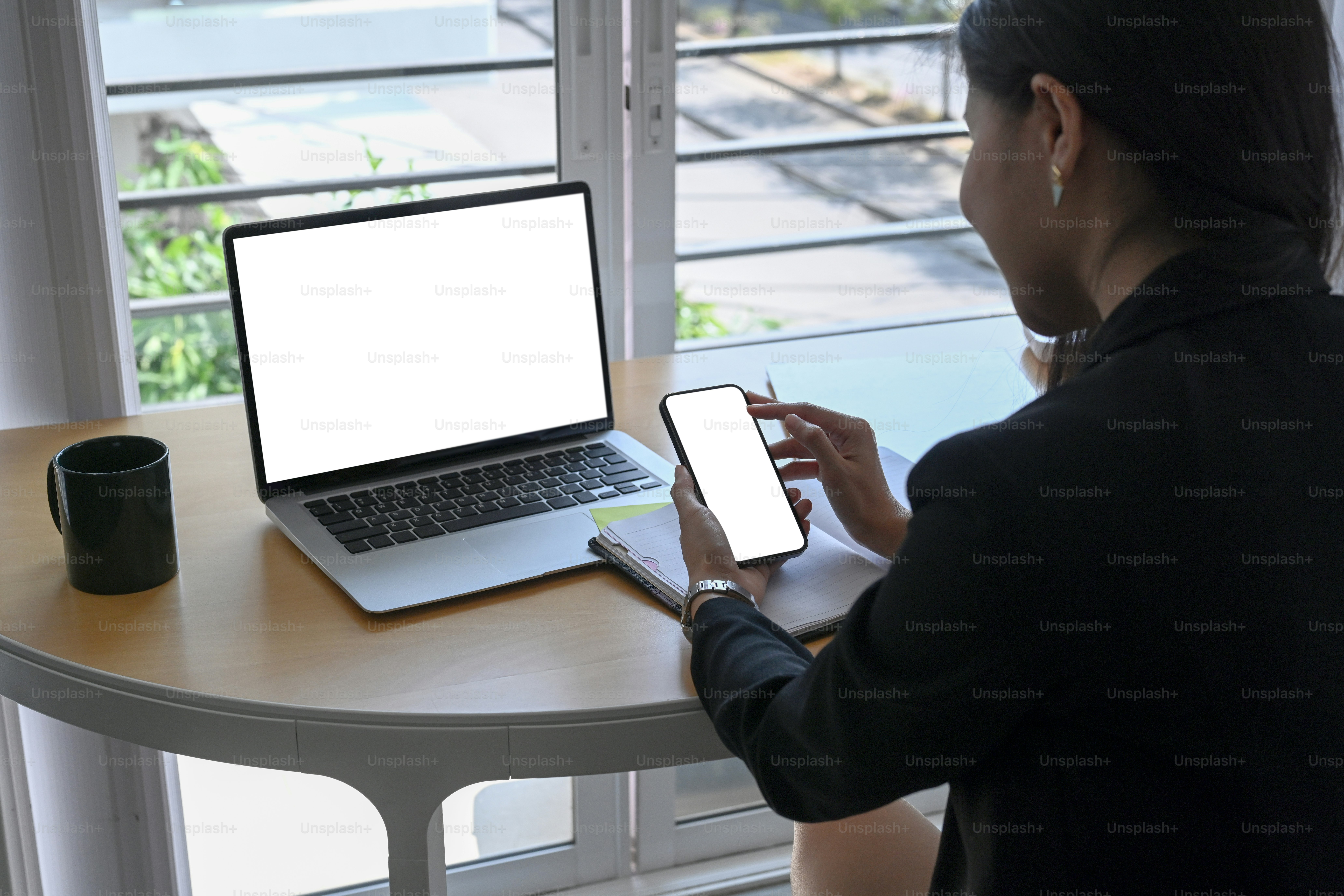 Rear view of businesswoman sitting near window in office and using smart phone.