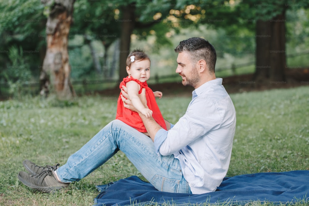 赤ん坊の娘と遊ぶ中年の白人自慢の父親。夏の日、公園の屋外で一緒に座っている家族のお父さんと娘。子供との生活。幸せなライフスタイルの2人家族。