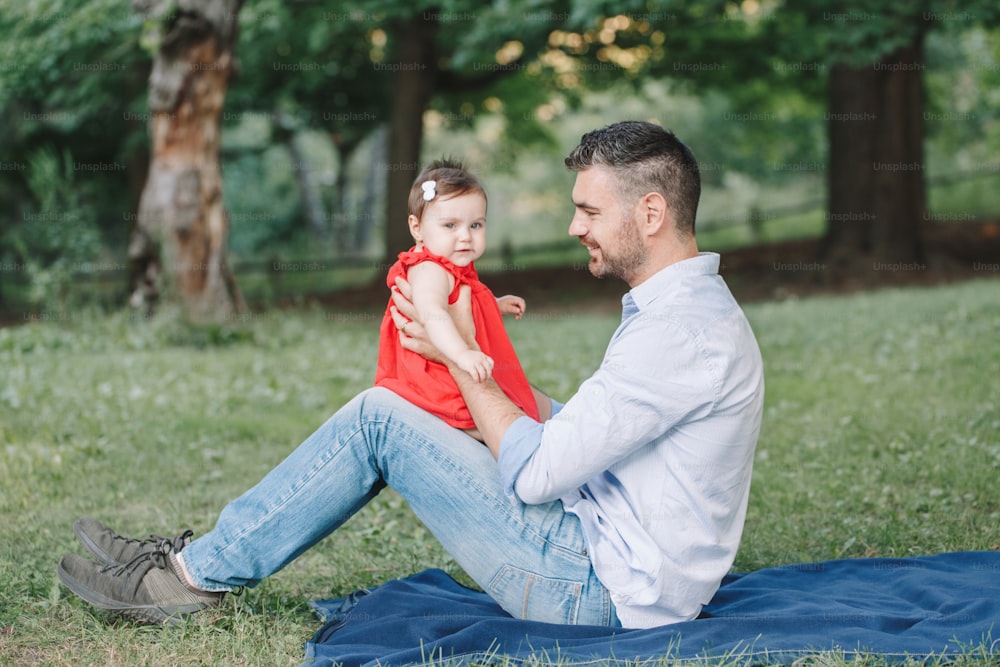 Middle age Caucasian proud father playing with baby daughter. Family dad and daughter sitting together outdoors in park on summer day. Life with kids children. Happy lifestyle family of two.