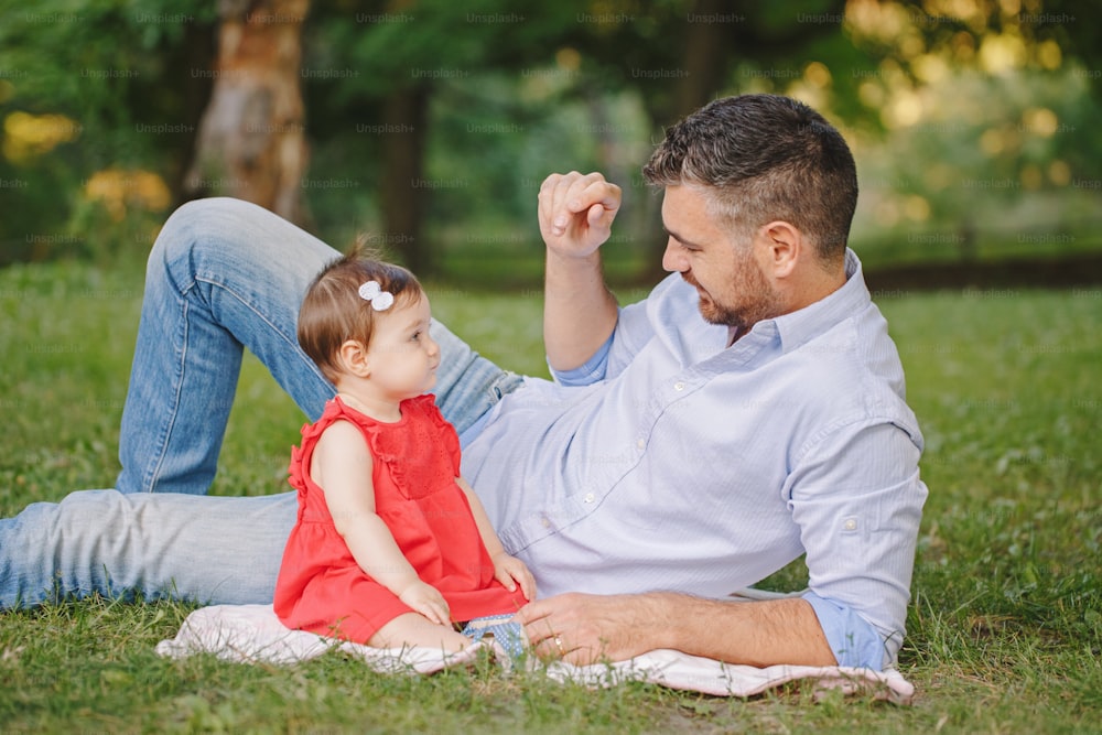 Middle age Caucasian proud father playing with baby daughter. Family dad and daughter sitting together outdoors in park on summer day. Life with kids children. Happy lifestyle family of two.