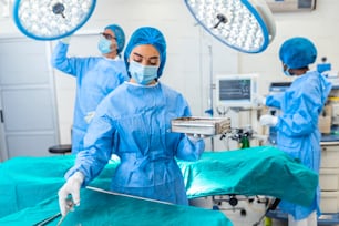 手術室で手術器具を手に取る手術服姿の女性外科医。病院の手術室にいる若い女性医師