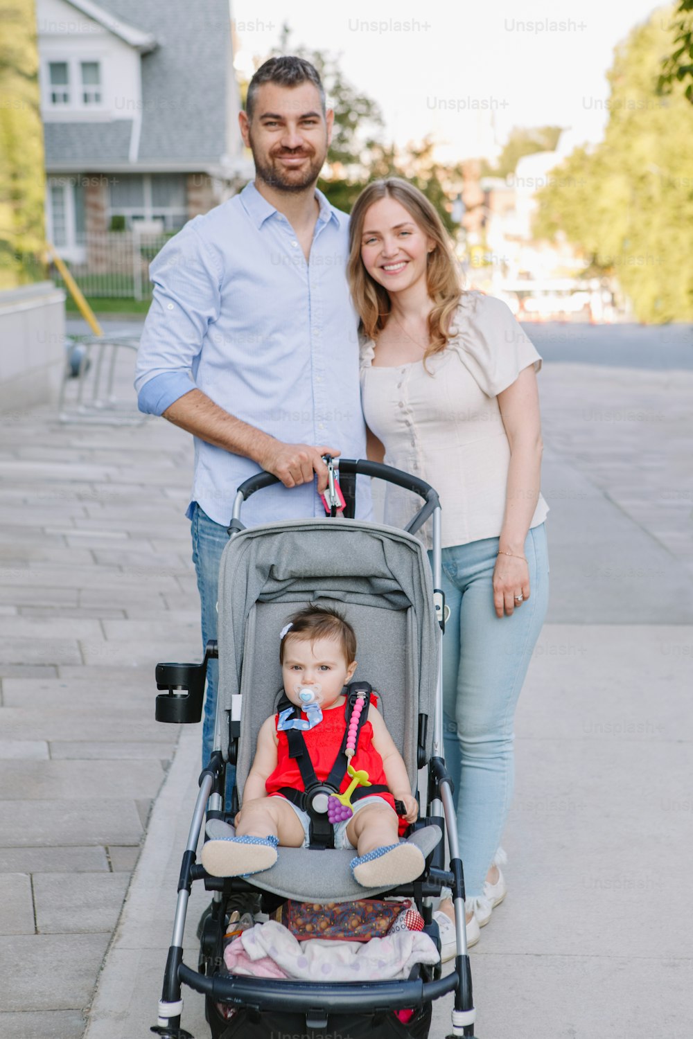 Caucasian mother and father walking with baby daughter in stroller. Family strolling together outdoor on city street on summer day. Urban life with kids children. Happy lifestyle family.