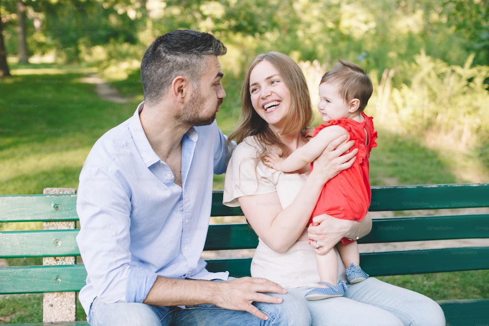 Caucasian smiling laughing mother and father with baby daughter in park. Happy family mom, dad and little girl together outdoor on summer day.