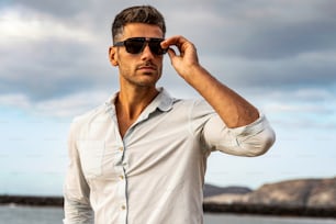 Magnifique homme élégant portant une chemise à la mode et des lunettes de soleil. Style citadin. Bel et charmant homme posant à l’extérieur. Lumière d’été.