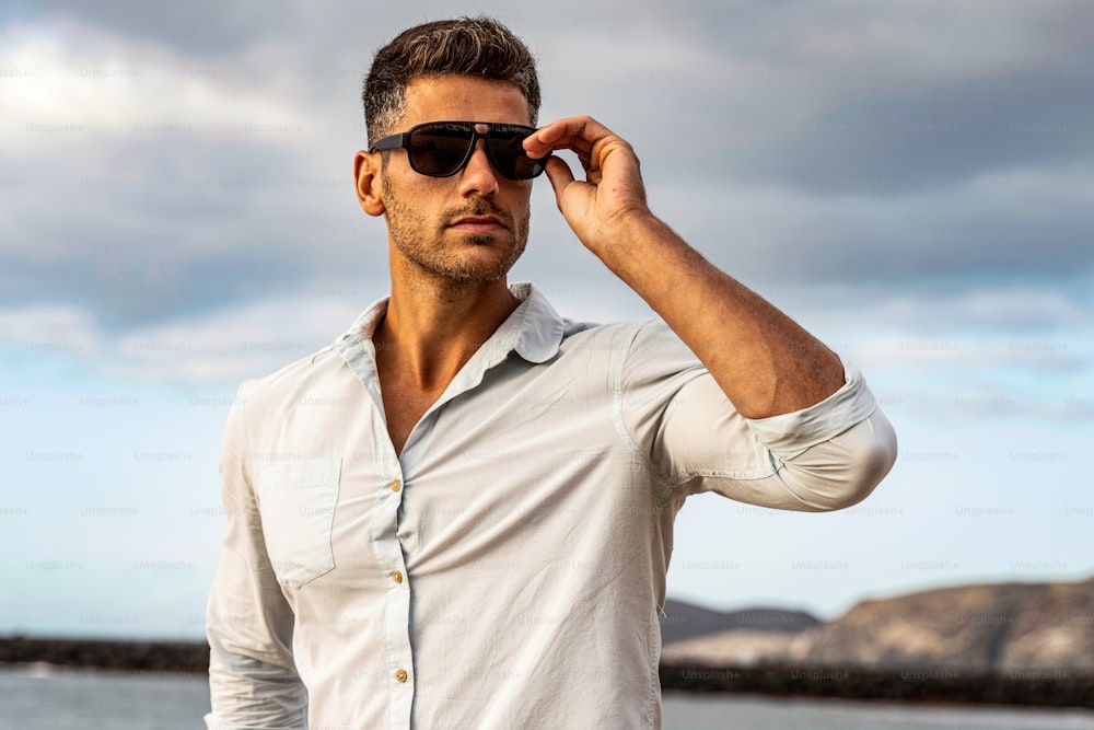 Gorgeous stylish man wearing fashionable shirt and sunglasses. City style. Beautiful and charming man posing outdoors. Summer light.