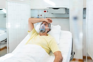 Porträt eines pensionierten älteren Mannes, der während des Coronavirus-Covid-19-Ausbruchs langsam mit Sauerstoffmaske atmet. Alter kranker Mann liegt im Krankenhausbett und wird wegen tödlicher Infektion behandelt