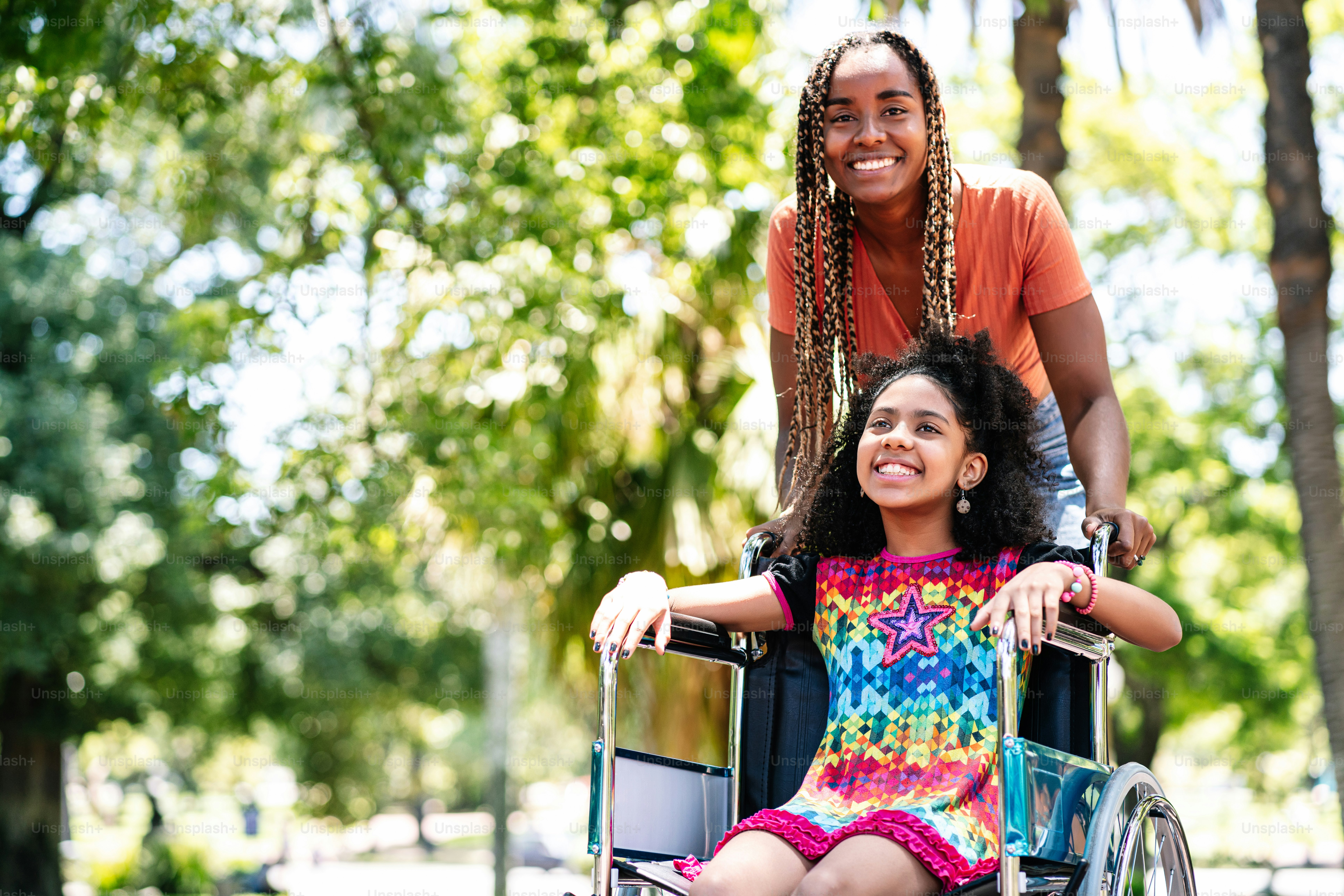 A little girl in a wheelchair enjoying a walk at the park with her ...