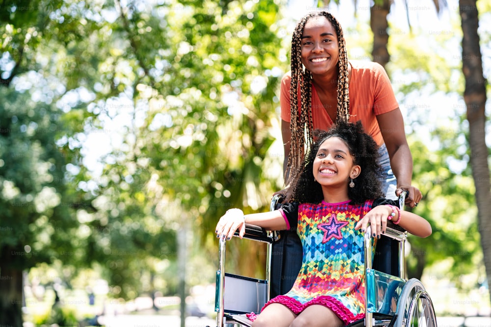 A little girl in a wheelchair enjoying a walk at the park with her mother.
