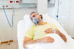 In the Hospital Senior covid-19 Patient Rests, Lying on the Bed with oxygen mask. Recovering Man Sleeping in the Modern Hospital Ward.