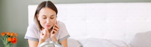 Middle age Caucasian woman applying makeup decorative cosmetics and talking on phone. Woman sitting in bed at home doing morning routine and chatting with friend. Web banner header.