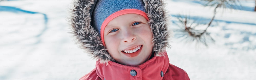 Cute adorable happy Caucasian smiling girl in pink jacket with fur hood during cold winter day. Kids outdoor seasonal activity. Funny face. Winter child portrait outside. Web banner header.
