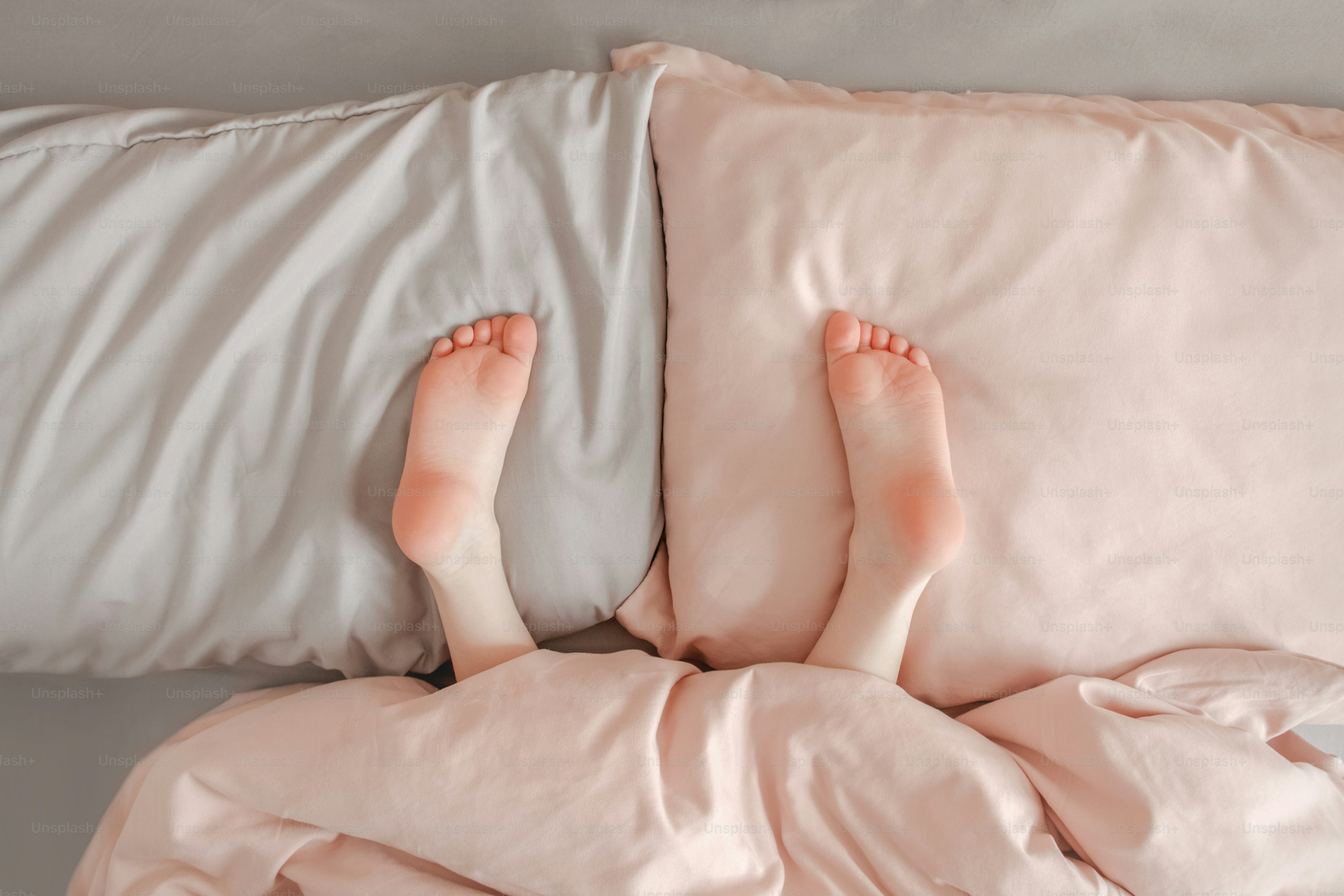 Bambini, gambe, piedi, piedi sdraiati sui cuscini a letto a casa. Bambino che gioca a nascondino sotto la coperta. Tacchi rosa adorabili a testa in giù a letto. Felice stile di vita autentico dell'infanzia.