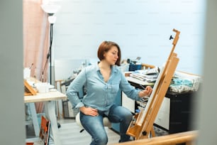自宅のアートスタジオでキャンバスに鉛筆で絵を描いている集中した中年の白人女性アーティスト。ライフスタイル活動、趣味。ユニークな職業。絵を描くアートフリーランサー。デジタルデトックス。