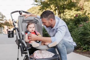 Caucasian proud father walking with baby daughter in stroller. Family dad and daughter together outdoor in city street on summer day. Urban life with kids children. Happy lifestyle family.