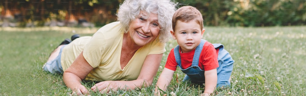 Grandmother with grandson boy at home backyard. Bonding of relatives and generation communication. Old woman with baby having fun spending time together outdoor. Web banner header.