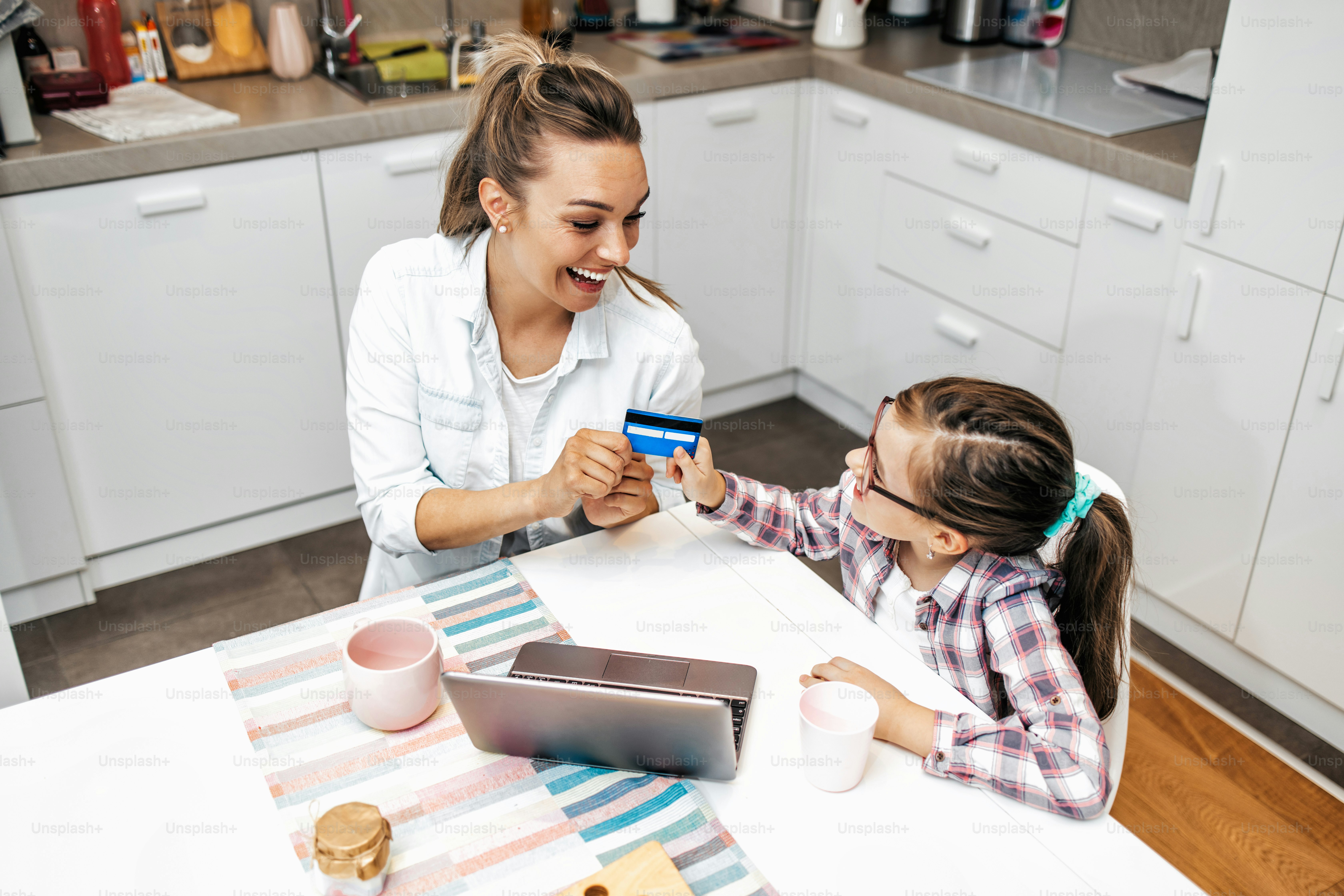 Happy mother with her young daughter enjoying in online shopping or working from home. Business from distance and virtual communication with family and friends.