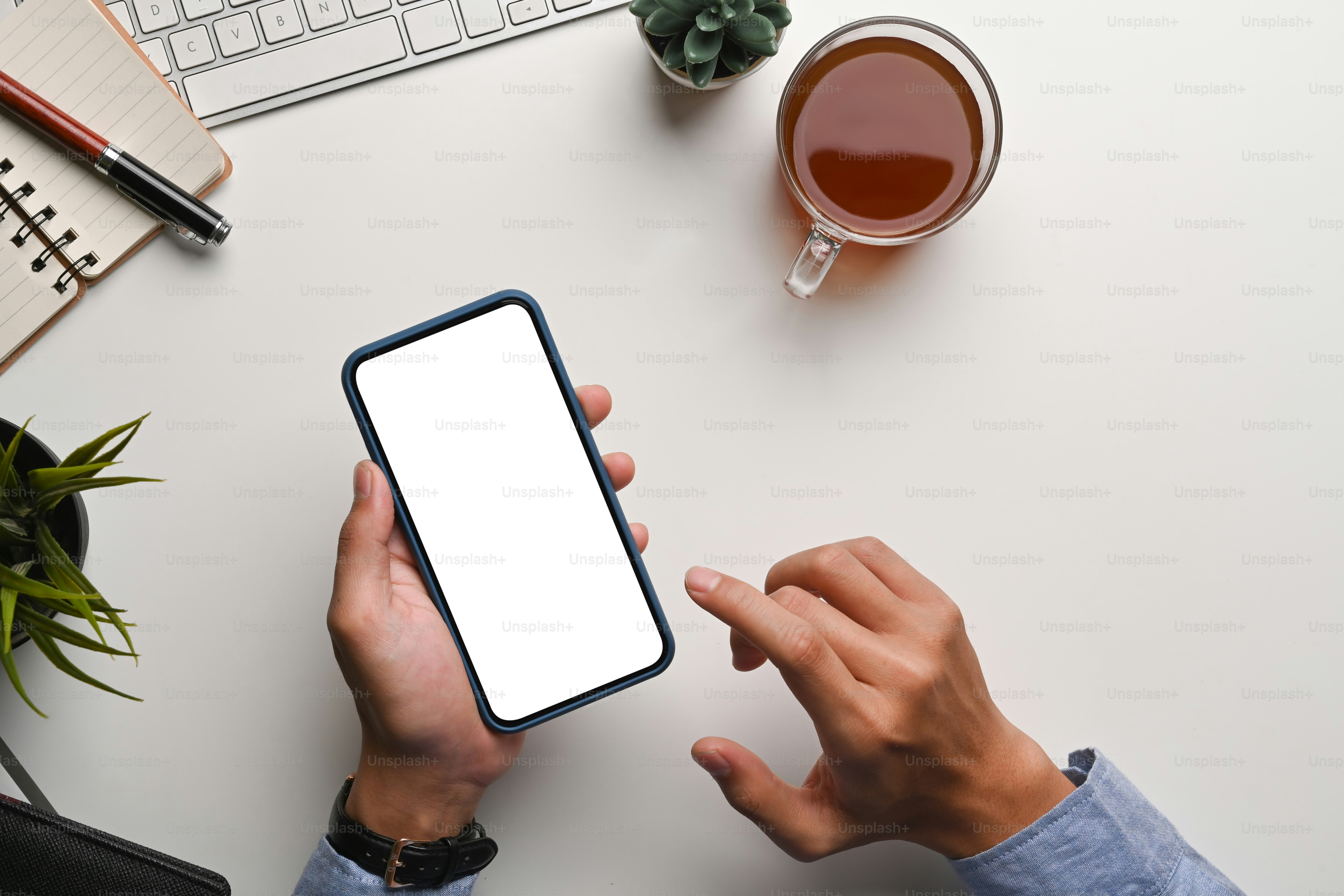 Top view of man holding mock up smart phone with blank screen on white office desk.