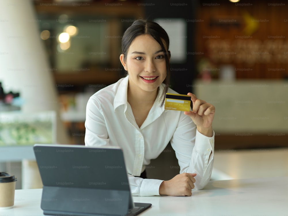 Retrato de una mujer de negocios que muestra la tarjeta de crédito a la cámara mientras está sentada en el lugar de trabajo