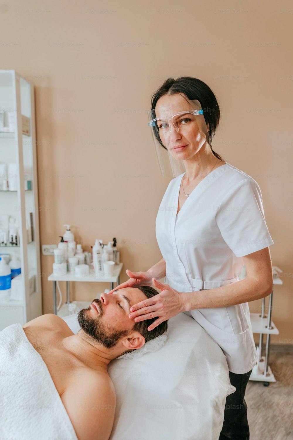 Kosmetikerin oder Gesichtspflegerin gibt einem Mann eine entspannende Gesichtsmassage