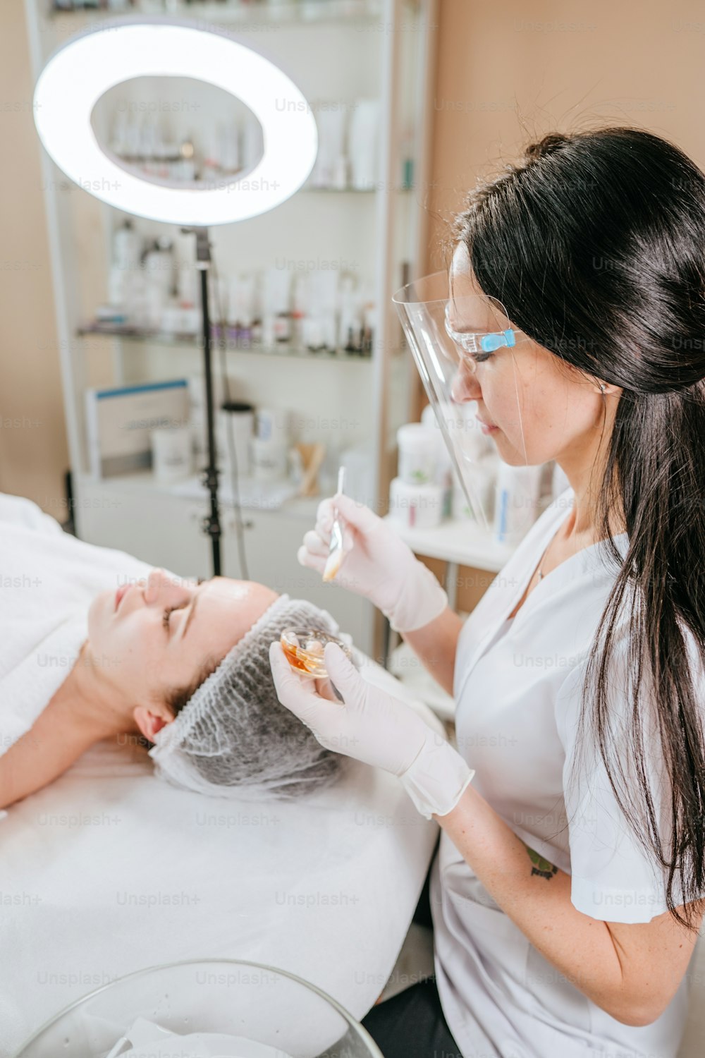 Esthetician or facialist making facial cleansing procedure to a woman in a beauty salon