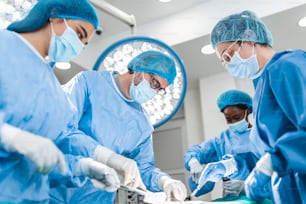 Vielfältiges Team von professionellen Chirurgen, Assistenten und Krankenschwestern, die invasive Operationen an einem Patienten im Operationssaal des Krankenhauses durchführen. Chirurgen sprechen und benutzen Instrumente. Echtes modernes Krankenhaus.