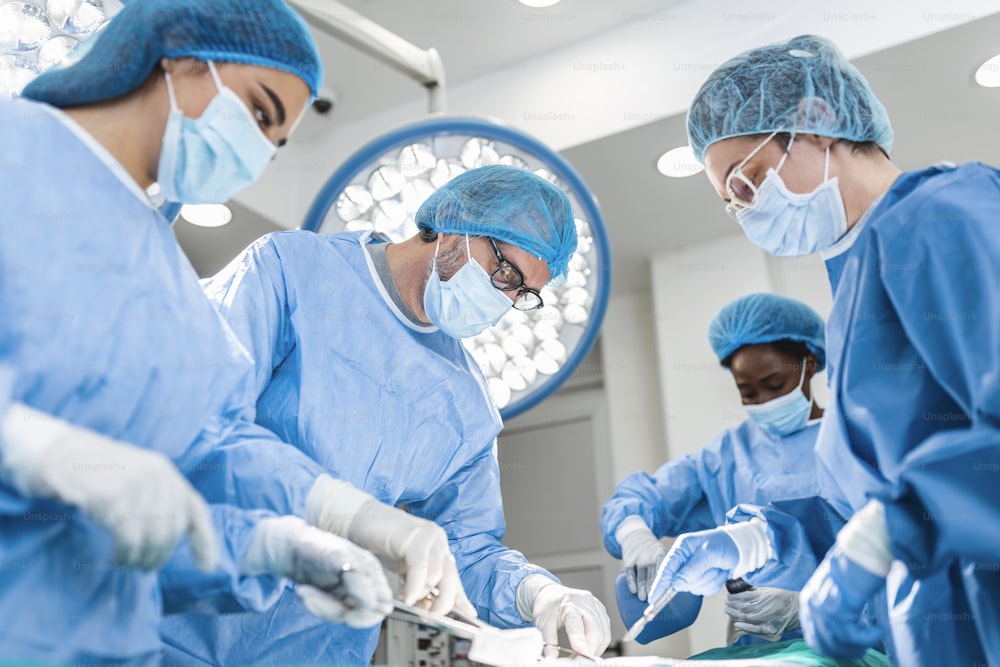 Équipe diversifiée de chirurgiens professionnels, d’assistants et d’infirmières effectuant une chirurgie invasive sur un patient dans la salle d’opération de l’hôpital. Les chirurgiens parlent et utilisent des instruments. Véritable hôpital moderne.