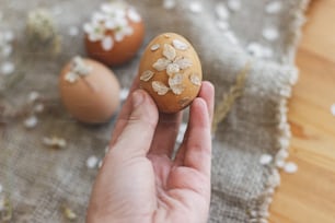 Mão segurando ovo de Páscoa decorado com pétalas de flores secas no fundo de guardanapo de linho rústico e flor de cereja. Decoração ecológica natural criativa de ovos de páscoa. Feliz Páscoa