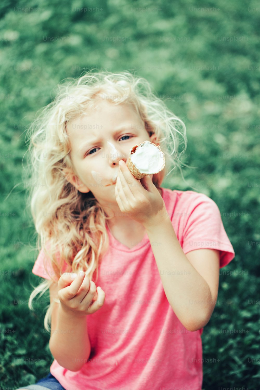 Cute funny adorable girl with long blonde messy hair eating licking ice cream from waffle cone. Child eating tasty sweet cold summer food outdoor. Summer frozen meal snack.