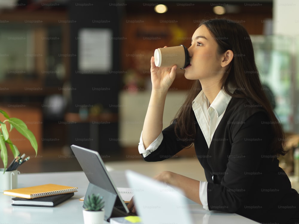 Portrait of businesswoman in black suit drinking coffee while sitting at workplace