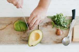 Young man cutting avocado top view on wooden cutting board. Perfectly ripe avocado in hands, making toasts in modern white kitchen. Healthy eating and Home cooking concept.