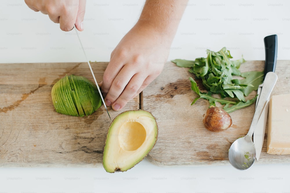 Young man cutting avocado top view on wooden cutting board. Perfectly ripe  avocado in hands, making toasts in modern white kitchen. Healthy eating and  Home cooking concept. photo – Food Image on
